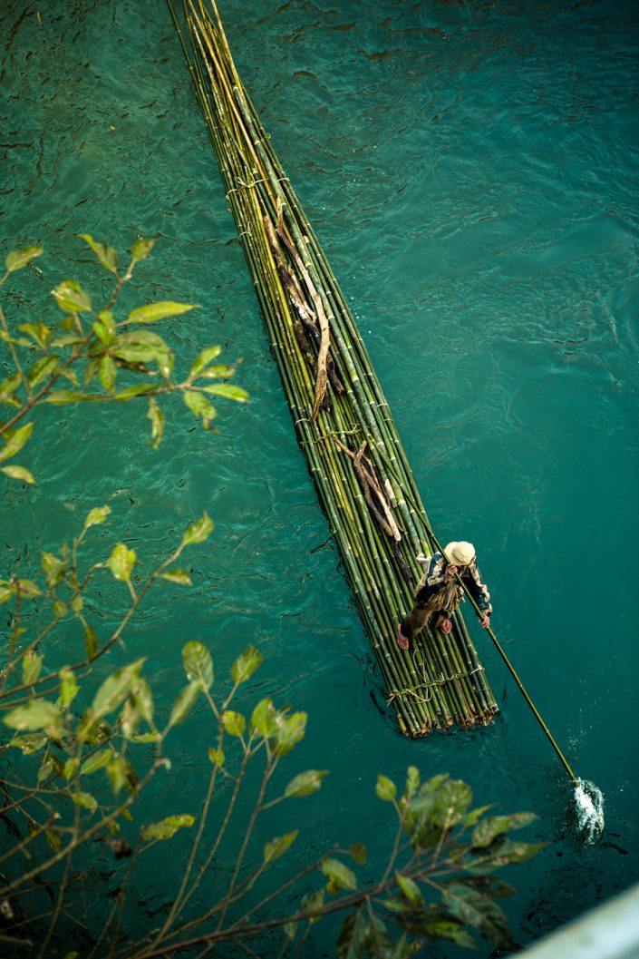 Man on green bamboo raft rows down river