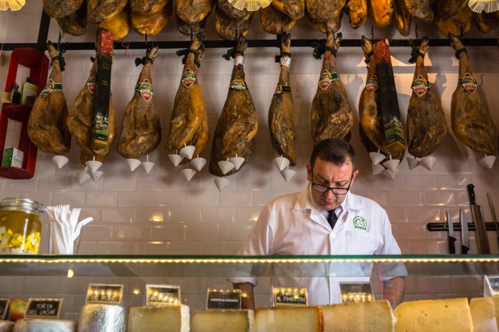 SEVILLE, SPAIN – AUG 2: Butcher stands in front of a wall of jam