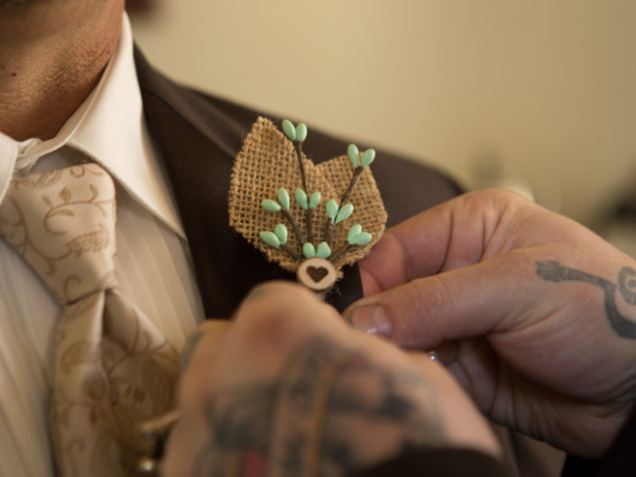 Tattooed hands pin burlap corsage on groom for wedding