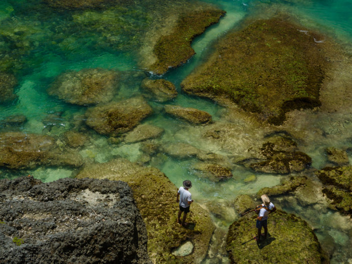 Two men stand on edge of crystal blue bay